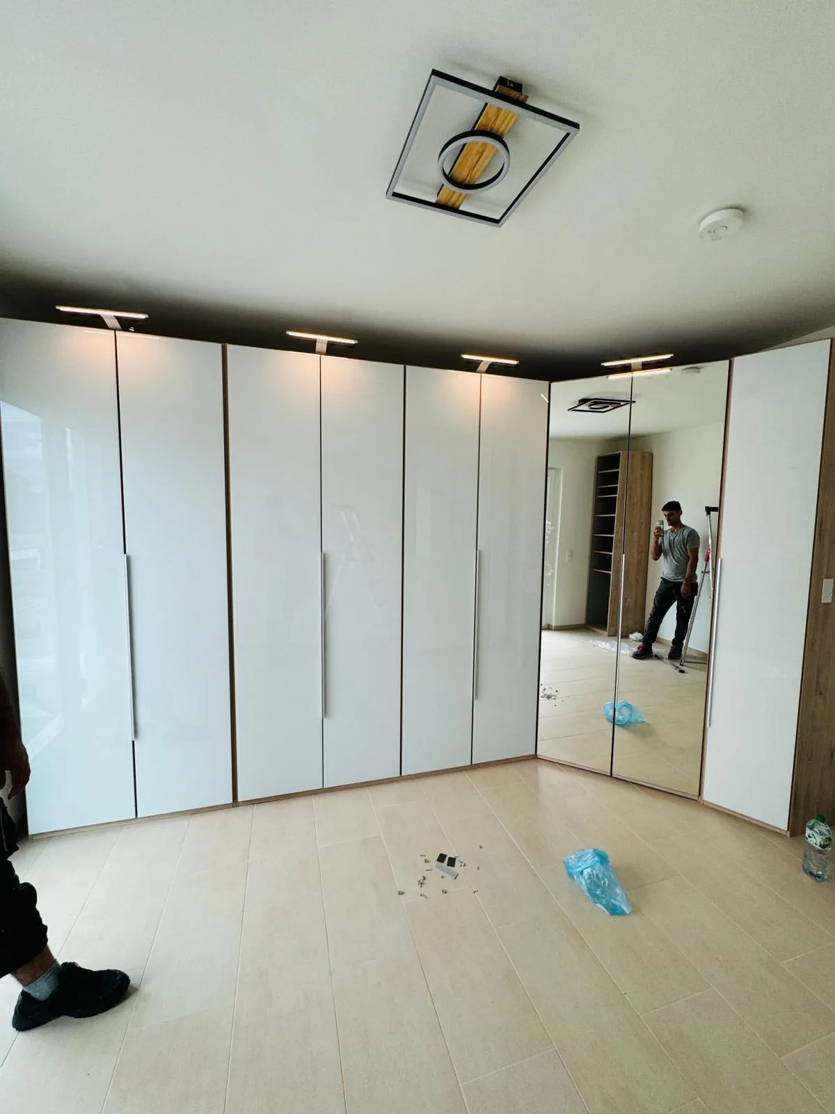 Fertig montierter weißer Eckkleiderschrank mit Spiegeltüren und Aufsatzleuchten, im Spiegel ein Mitarbeiter mit Leiter