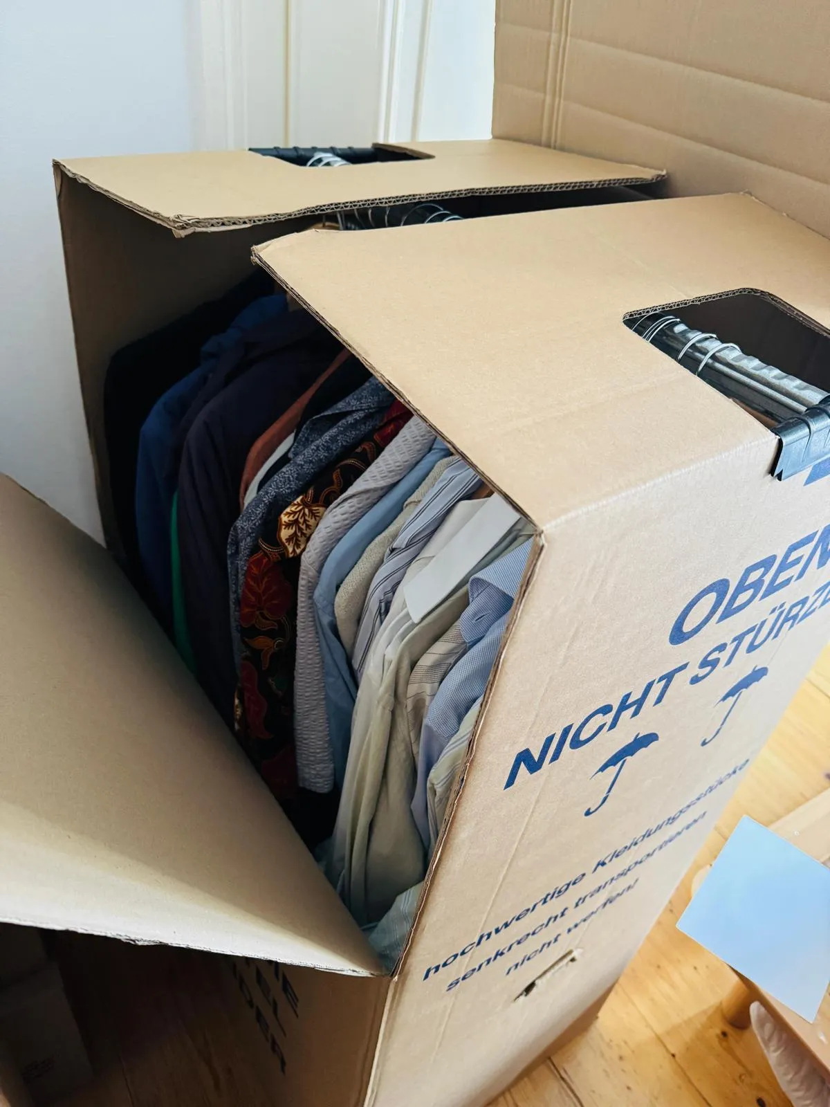 Geöffnete Kleiderbox mit Hemden und Jacken auf der Kleiderstange – so reist hängende Kleidung ohne Falten in die neue Wohnung