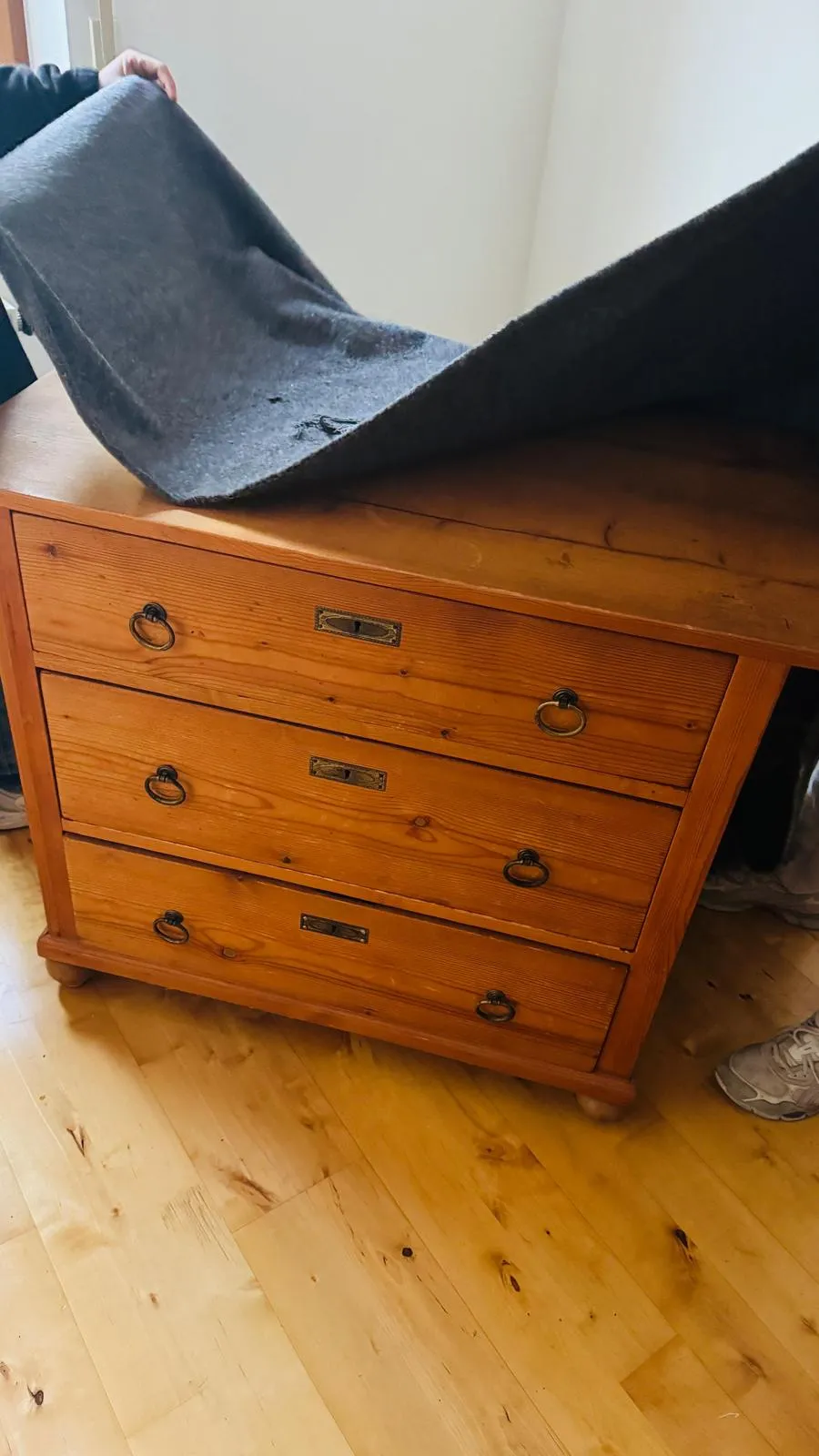 Eine alte Holzkommode mit Messinggriffen wird vor dem Transport mit einer grauen Umzugsdecke abgedeckt