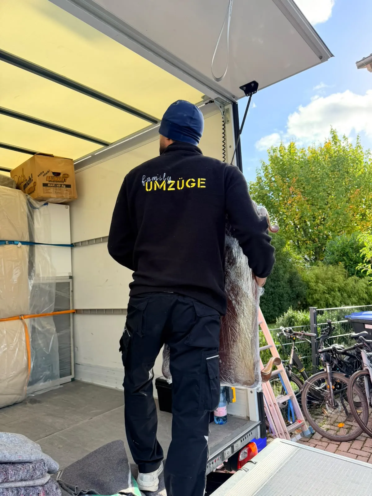 Mitarbeiter von Family Umzüge hebt ein in Folie gewickeltes Möbelteil in den Umzugswagen, im Laderaum stehen bereits verpackte Möbel