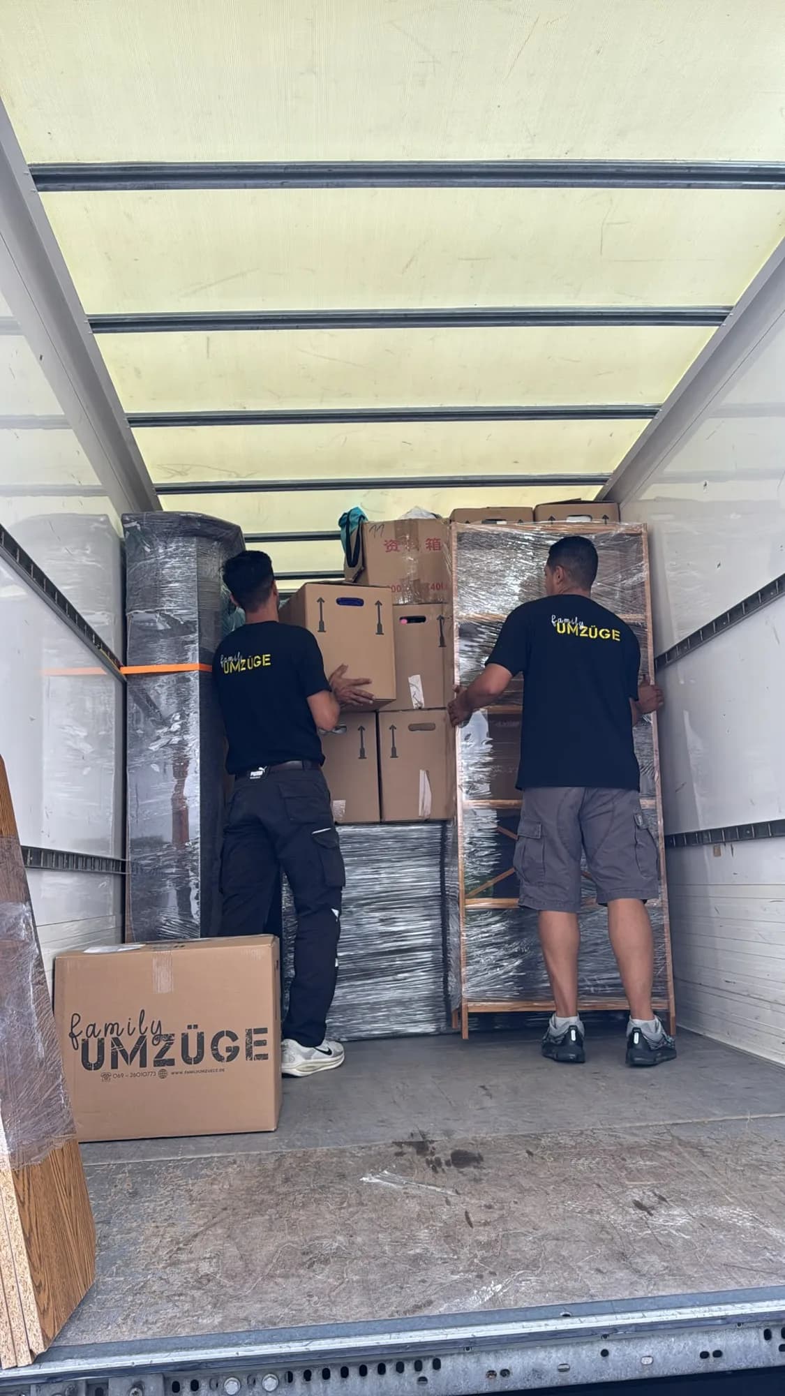 Zwei Mitarbeiter von Family Umzüge verstauen Kartons und ein Regal sicher im Umzugs-Lkw