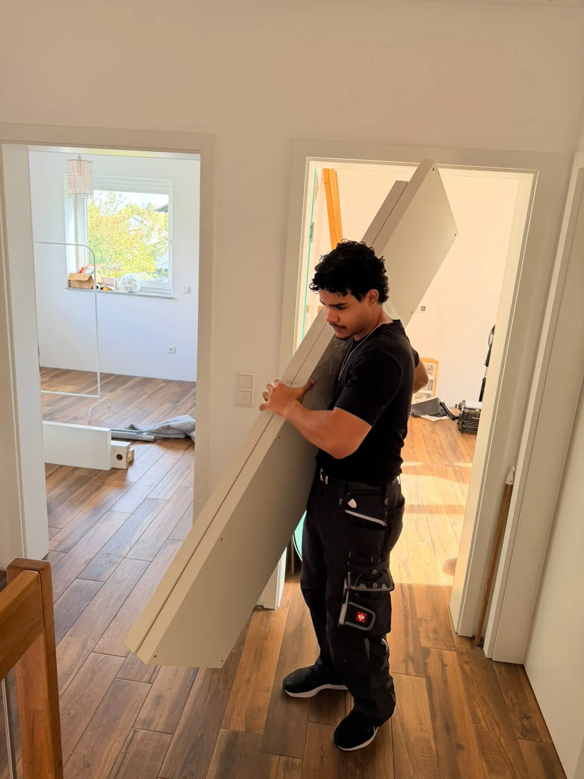 Mitarbeiter von Family Umzüge trägt eine abgebaute weiße Schrankseite durch den Flur einer Wohnung