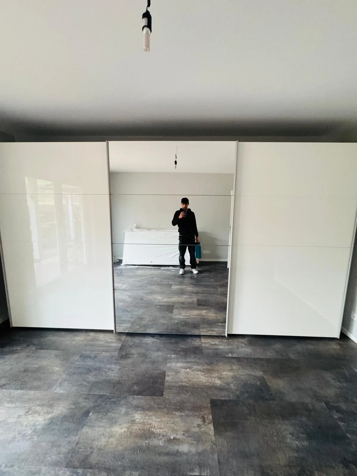 Fertig montierter weißer Schwebetürenschrank mit Spiegeltür, im Spiegel der Mitarbeiter mit seinem Werkzeugkoffer