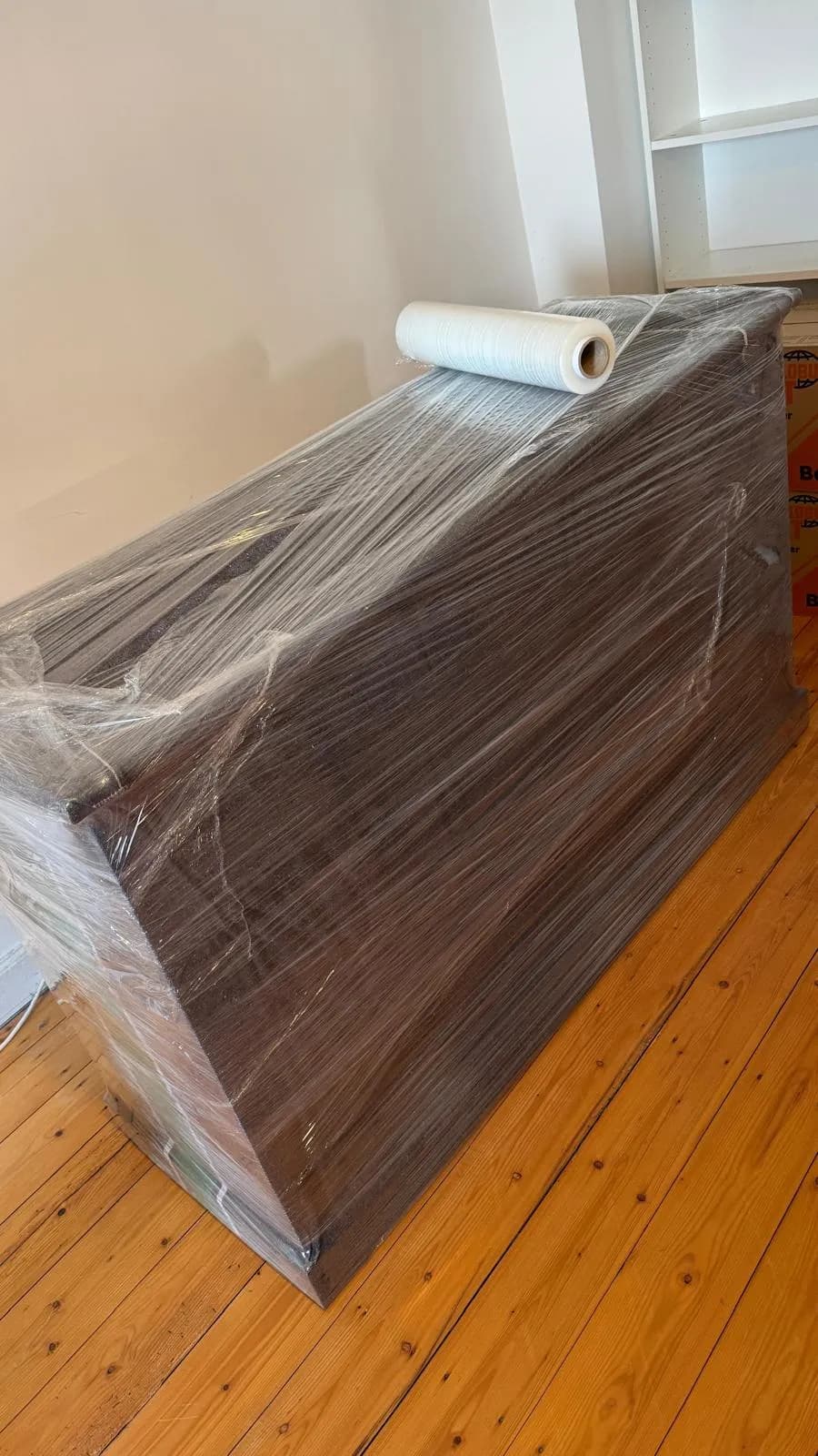 Dunkles Sideboard in mehreren Lagen Stretchfolie verpackt, obenauf liegt die Folienrolle, im Hintergrund leere Regale