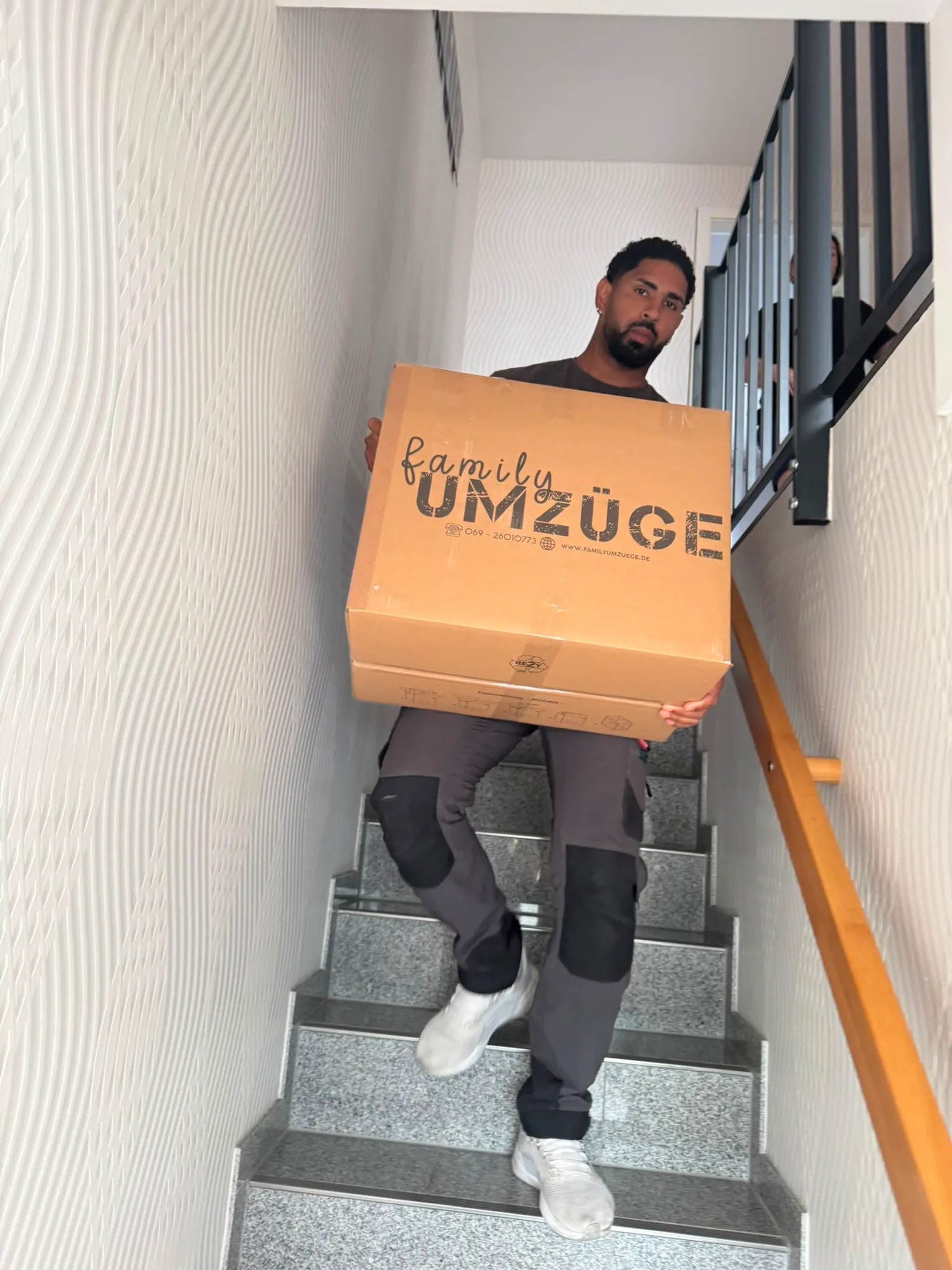 Mitarbeiter von Family Umzüge trägt einen beschrifteten Family-Umzüge-Karton durchs Treppenhaus – entspannter Privatumzug in Frankfurt