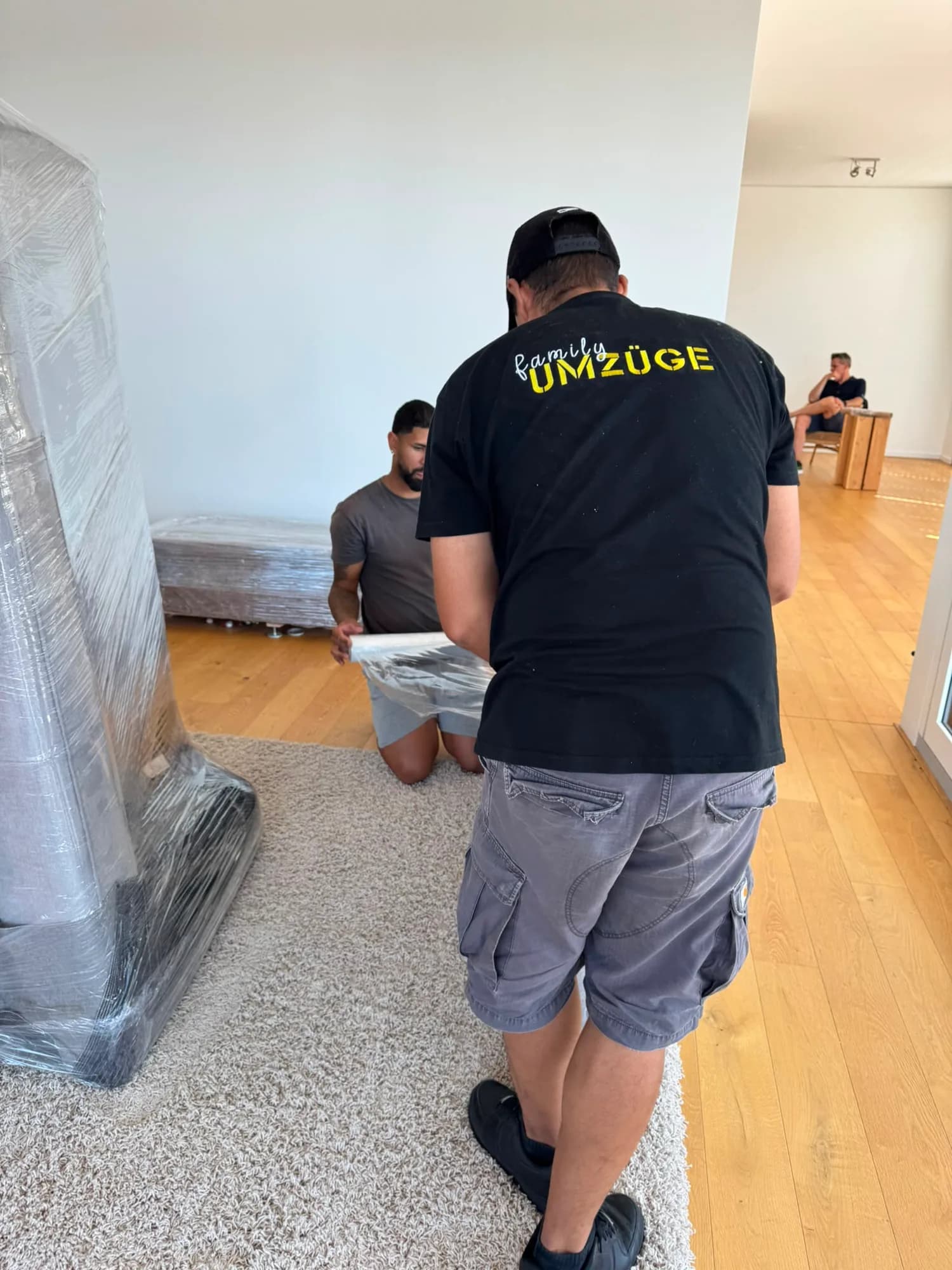 Zwei Mitarbeiter von Family Umzüge verpacken Möbel, während der Kunde entspannt im Hintergrund sitzt