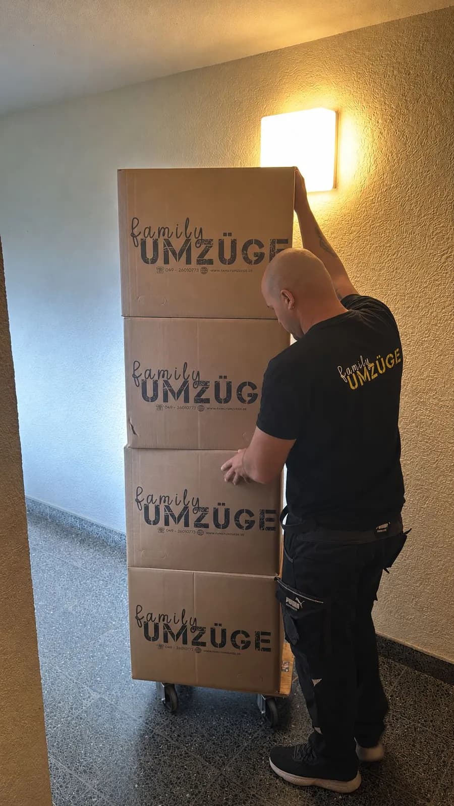 Mitarbeiter von Family Umzüge transportiert beschriftete Umzugskartons auf einer Sackkarre durch ein Treppenhaus