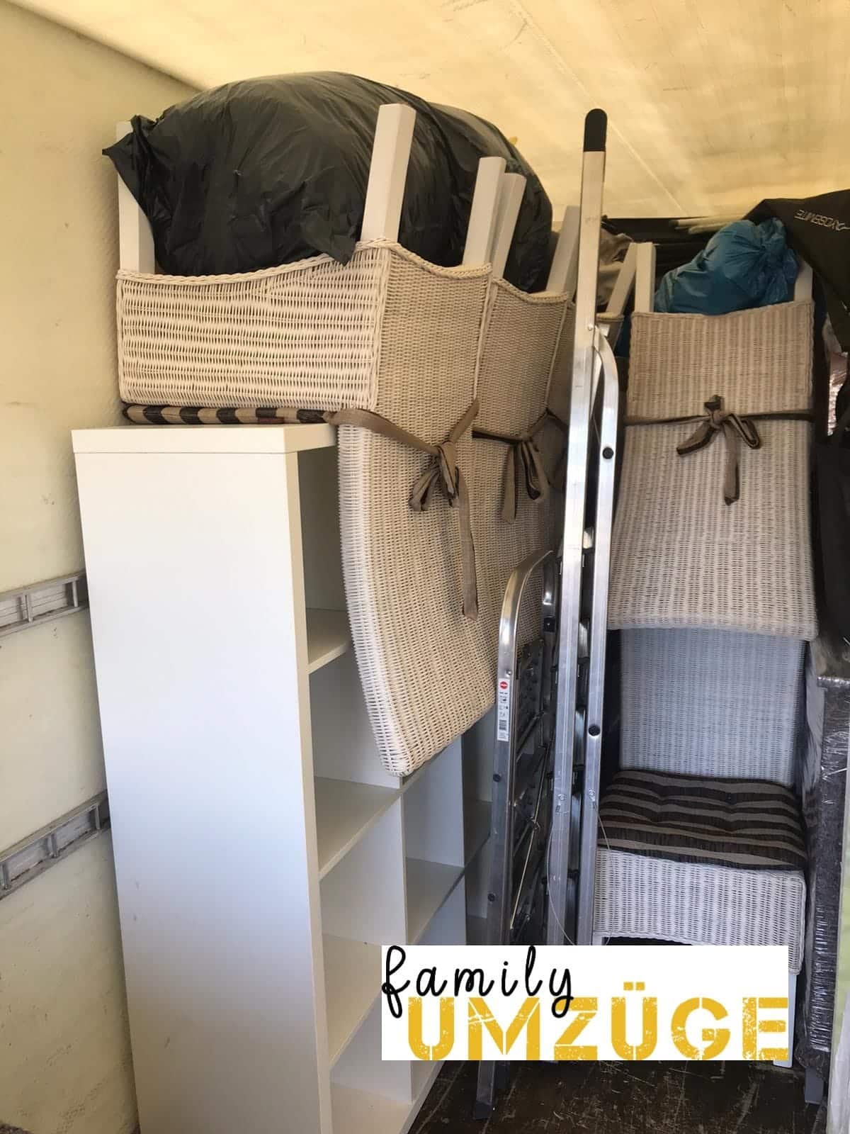 Ein Umzugswagen, vollgepackt mit Möbeln, darunter weiße Regale, Weidenkörbe, Stühle, Taschen und eine Metallleiter. In der unteren rechten Ecke ist das Logo von Familie UMZÜGE zu sehen, einem Umzugsunternehmen, auf das sich die Frankfurter verlassen. - Family Umzüge